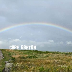 Full rainbow over the Inverness boardwalk and town in Cape Breton, Nova Scotia, with bold CAPE BRETON lettering