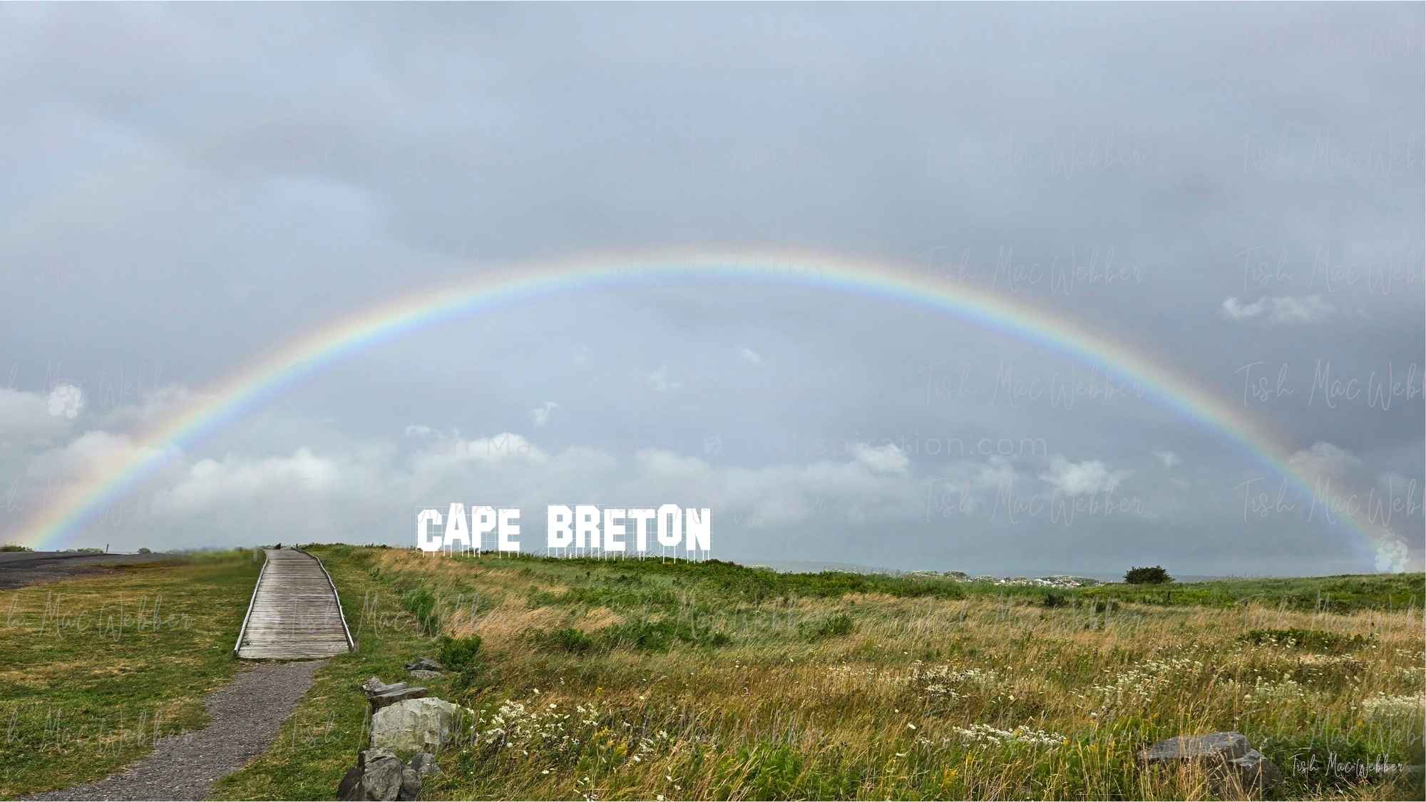 Full rainbow over the Inverness boardwalk and town in Cape Breton, Nova Scotia, with bold CAPE BRETON lettering