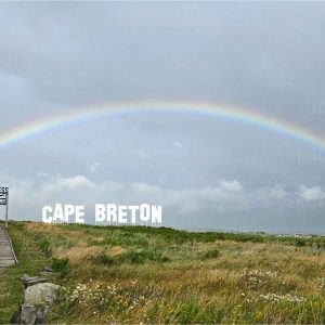 Full rainbow over the Inverness boardwalk and town with the Inverness sign and bold CAPE BRETON lettering