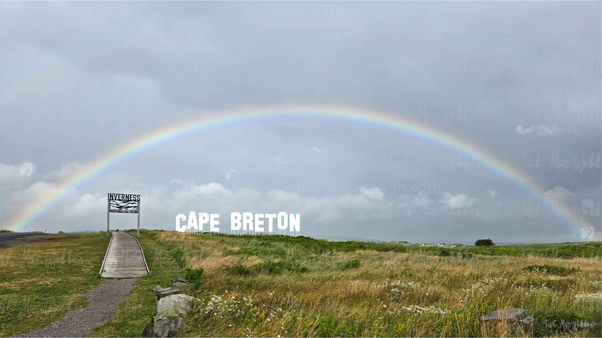 Full rainbow over the Inverness boardwalk and town with the Inverness sign and bold CAPE BRETON lettering