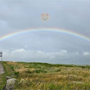 Full rainbow over the Inverness boardwalk and town with the Inverness sign and three smiling emojis with heart eyes, star eyes, and sunglasses floating over the rainbow.