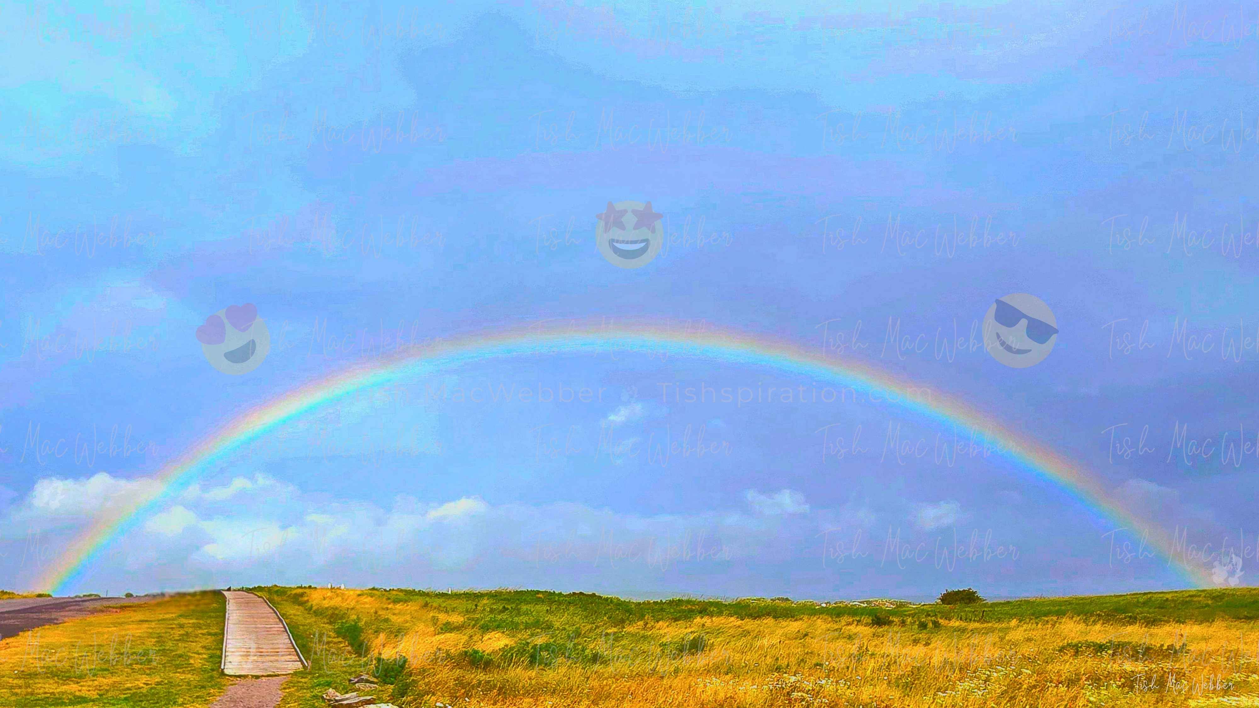 Full rainbow over the Inverness boardwalk and town in Cape Breton, Nova Scotia, with three smiling emojis with heart eyes, star eyes, sunglasses floating over the rainbow.