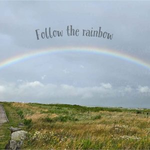 Full rainbow over the Inverness boardwalk and town in Cape Breton, Nova Scotia, with the words Follow the rainbow and HOME