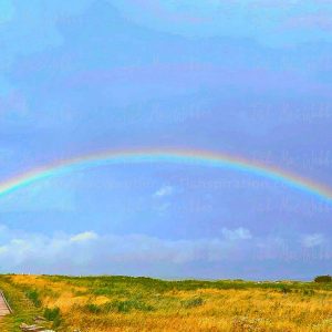 Vivid full rainbow over the Inverness boardwalk and town in Cape Breton, Nova Scotia, with the Inverness sign