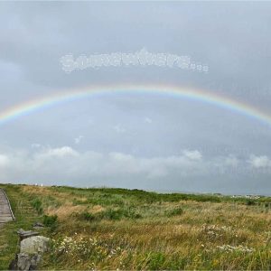 Full rainbow over the Inverness boardwalk and town in Cape Breton, Nova Scotia, with the word Somewhere above the rainbow