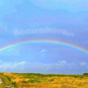 Vivid full rainbow over the Inverness boardwalk and town in Cape Breton, Nova Scotia, with the Inverness sign and the word Somewhere above the rainbow